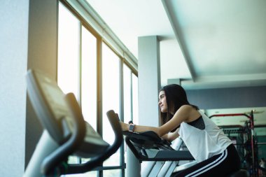 Spor salonunda egzersiz bisikleti kullanan zinde bir genç kız. Spor salonunda jimnastik yapan bir kadın..