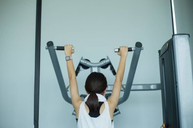 Genç fitness kızı spor salonunda egzersiz makinesiyle egzersiz yapıyor.