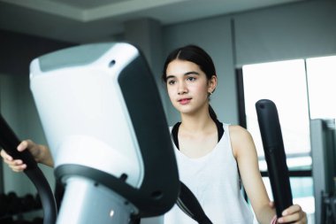 Spor salonunda Eliptik Egzersiz yapan Asyalı kız spor yapıyor. Zayıf ve sağlıklı yaşam tarzı için makine aerobiğiyle kilo veriyor.