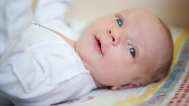 Portre. Yakın plan. Beyaz elbiseli bebek sırt üstü yatar ve ellerini sallar..