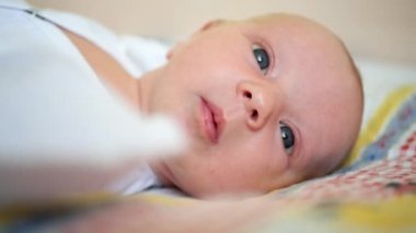 Portre. Yakın plan. Beyaz elbiseli bebek sırt üstü yatar ve ellerini sallar..