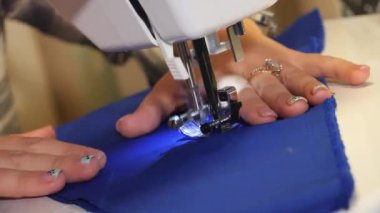 Yakın plan. Terzi dikiş makinesine mavi kumaş dikiyor. Evde elbise dikiyorum..