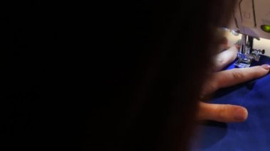 Bir terzi dikiş makinesine mavi bir kumaş diker. Kamera soldan sağa hareket ediyor..