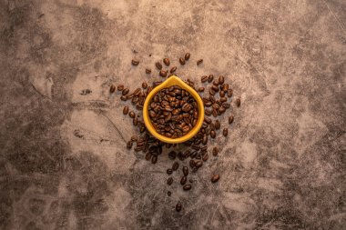 Renkli sarı fincanın içinde taze taze çiğ organik kahve çekirdekleri tahta tezgahta duruyor.