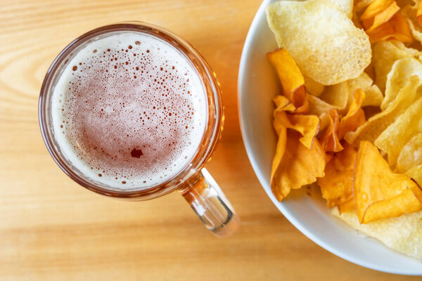 Mug with beer and chips on a wooden table.