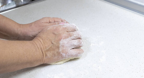 Hands of granny kneads dough. 60 years old woman hands kneading dough. Grandmother dough molding on table. Wheat homemade baking. Pastry and cookery.