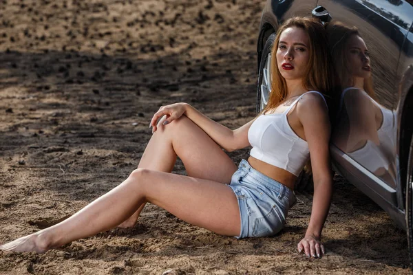 Blonde in top and shorts sitting near the car — Stock Photo, Image