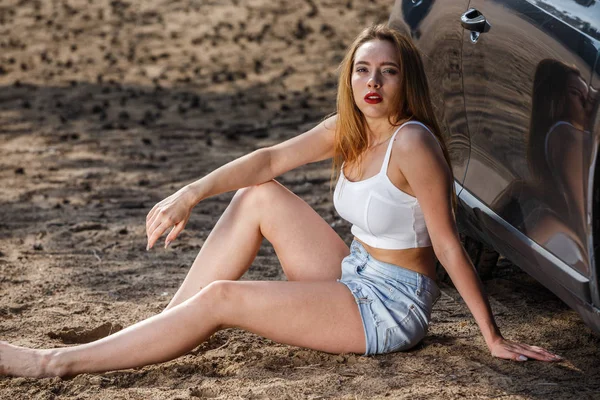 Blonde in top en shorts zitten in de buurt van de auto — Stockfoto