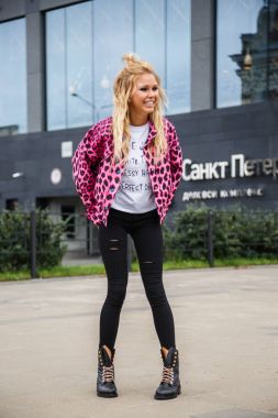 Pembe ceket ve açık havada ile ayakta siyah kot giyen güzel sarışın kadın alışveriş arka plan üzerinde bulanık