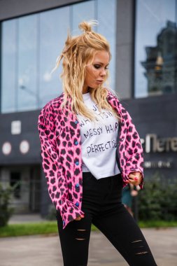 Pembe ceket ve açık havada ile ayakta siyah kot giyen güzel sarışın kadın alışveriş arka plan üzerinde bulanık