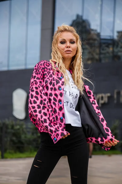 Pembe ceket ve açık havada ile ayakta siyah kot giyen güzel sarışın kadın alışveriş arka plan üzerinde bulanık