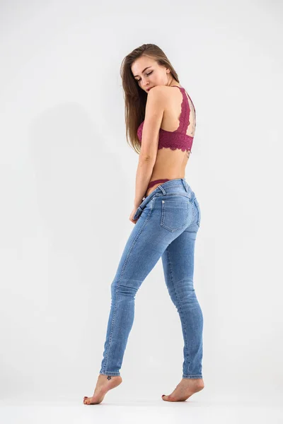 Vacker flicka blondin i underkläder och jeans poserar på vita bac — Stockfoto