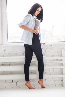 Stüdyo Daire iç pencerede yakınındaki koyu kot pantolon ve beyaz gömlek ayakta giyen güzel esmer kadın görüntüsünü