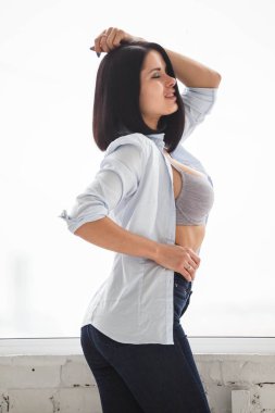 Stüdyo Daire iç pencerede yakınındaki koyu kot pantolon ve beyaz gömlek ayakta giyen güzel esmer kadın görüntüsünü