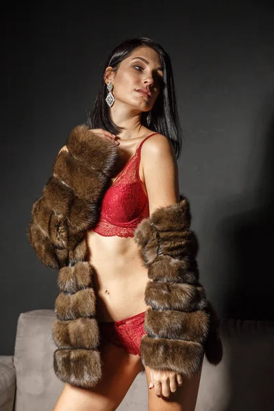 セクシーな赤いランジェリーの美しいブルネットの少女の肖像画スタジオ 若い女性のアパートのインテリアで毛皮のコートでのショット — ストック写真