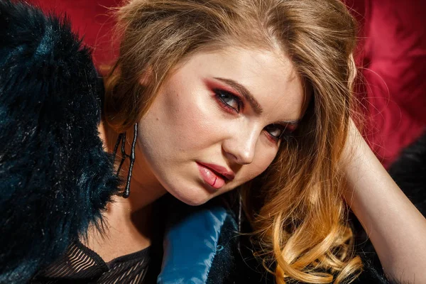 Portre güzellik modeli giymiş mavi ceket. Şık makyaj kırmızı kanepede yatan genç kadın