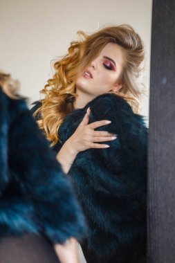 Stüdyo portre güzellik modeli giymiş siyah bluz ve mavi ceket. Aynaya bakarak şık makyaj ile genç kadın 