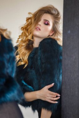 Stüdyo portre güzellik modeli giymiş siyah bluz ve mavi ceket. Aynaya bakarak şık makyaj ile genç kadın 