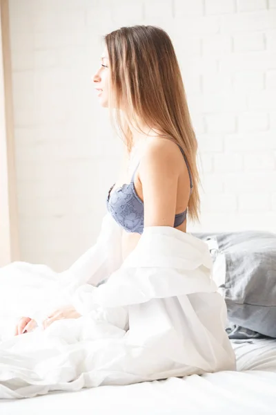 青いランジェリーを身に着けている美容女性のスタジオ撮影 ホーム インテリアの背景のベッドの上に座っている若い女性 — ストック写真