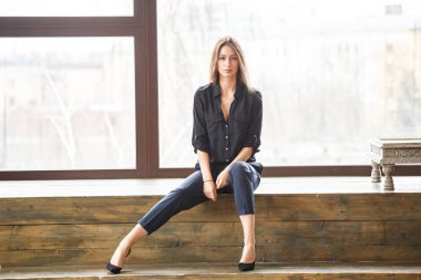 Ahşap zemin, ışıklı windows arka plan üzerinde oturan siyah rahat kıyafetler giymiş güzel genç kadın stüdyo çekim