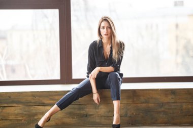 Ahşap zemin, ışıklı windows arka plan üzerinde oturan siyah rahat kıyafetler giymiş güzel genç kadın stüdyo çekim