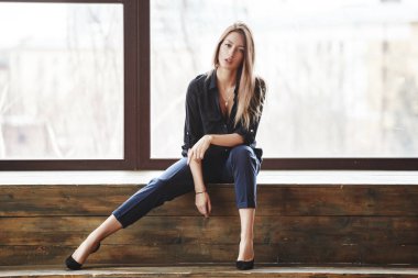 Ahşap zemin, ışıklı windows arka plan üzerinde oturan siyah rahat kıyafetler giymiş güzel genç kadın stüdyo çekim