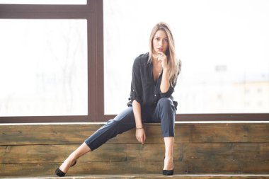 Ahşap zemin, ışıklı windows arka plan üzerinde oturan siyah rahat kıyafetler giymiş güzel genç kadın stüdyo çekim