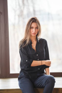 Ahşap zemin, ışıklı windows arka plan üzerinde oturan siyah rahat kıyafetler giymiş güzel genç kadın stüdyo çekim