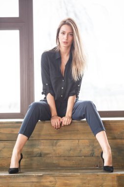 Ahşap zemin, ışıklı windows arka plan üzerinde oturan siyah rahat kıyafetler giymiş güzel genç kadın stüdyo çekim