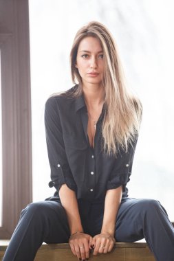 Ahşap zemin, ışıklı windows arka plan üzerinde oturan siyah rahat kıyafetler giymiş güzel genç kadın stüdyo çekim