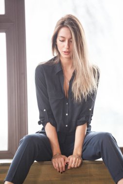 Ahşap zemin, ışıklı windows arka plan üzerinde oturan siyah rahat kıyafetler giymiş güzel genç kadın stüdyo çekim