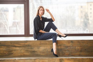 Ahşap zemin, ışıklı windows arka plan üzerinde oturan siyah rahat kıyafetler giymiş güzel genç kadın stüdyo çekim