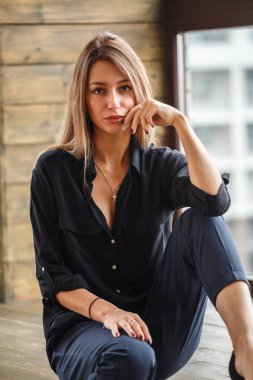 Ahşap zemin, ışıklı windows arka plan üzerinde oturan siyah rahat kıyafetler giymiş güzel genç kadın stüdyo çekim