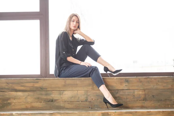 木製の床 明かりのついた窓の背景に座って黒のカジュアルな服を着ての美しい若い女性のスタジオ撮影 — ストック写真