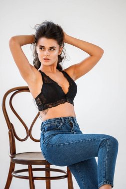 Kot ve beyaz duvar arka plan ahşap sandalyede oturan cinsel siyah iç çamaşırı giyen güzel kıvırcık esmer kız portresi stüdyo