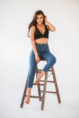 Mavi jeans ve Ahşap merdiven, beyaz duvar arka plan eğilerek cinsel siyah iç çamaşırı giyen güzel kıvırcık esmer kız portresi stüdyo