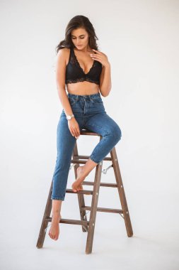 Mavi jeans ve Ahşap merdiven, beyaz duvar arka plan eğilerek cinsel siyah iç çamaşırı giyen güzel kıvırcık esmer kız portresi stüdyo
