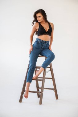 Mavi jeans ve Ahşap merdiven, beyaz duvar arka plan eğilerek cinsel siyah iç çamaşırı giyen güzel kıvırcık esmer kız portresi stüdyo