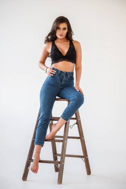 Mavi jeans ve Ahşap merdiven, beyaz duvar arka plan eğilerek cinsel siyah iç çamaşırı giyen güzel kıvırcık esmer kız portresi stüdyo