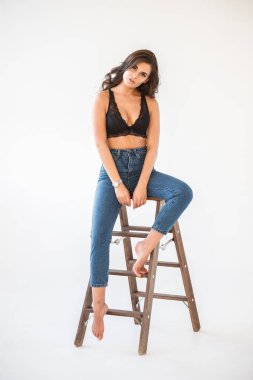Mavi jeans ve Ahşap merdiven, beyaz duvar arka plan eğilerek cinsel siyah iç çamaşırı giyen güzel kıvırcık esmer kız portresi stüdyo