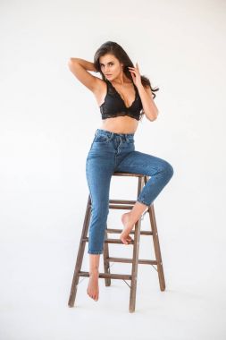 Mavi jeans ve Ahşap merdiven, beyaz duvar arka plan eğilerek cinsel siyah iç çamaşırı giyen güzel kıvırcık esmer kız portresi stüdyo