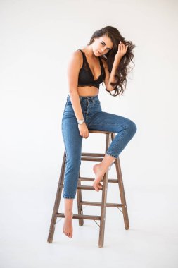 Mavi jeans ve Ahşap merdiven, beyaz duvar arka plan eğilerek cinsel siyah iç çamaşırı giyen güzel kıvırcık esmer kız portresi stüdyo