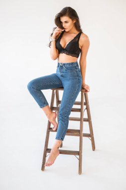 Mavi jeans ve Ahşap merdiven, beyaz duvar arka plan eğilerek cinsel siyah iç çamaşırı giyen güzel kıvırcık esmer kız portresi stüdyo