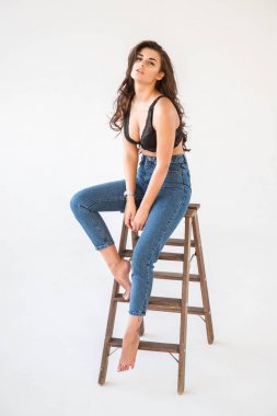 Mavi jeans ve Ahşap merdiven, beyaz duvar arka plan eğilerek cinsel siyah iç çamaşırı giyen güzel kıvırcık esmer kız portresi stüdyo