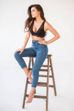 Mavi jeans ve Ahşap merdiven, beyaz duvar arka plan eğilerek cinsel siyah iç çamaşırı giyen güzel kıvırcık esmer kız portresi stüdyo