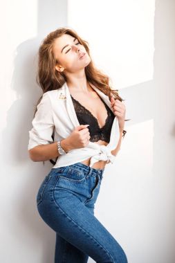 Mavi kot pantolon, beyaz gömlek ve siyah iç çamaşırı cinsel ayakta beyaz duvar arka plan üzerinde giyen güzel kıvırcık esmer kız portresi stüdyo