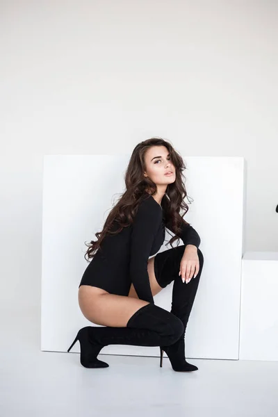 セクシーなブルネット少女が黒いランジェリーと白い背景の上に座ってブーツのスタジオ ポートレート — ストック写真