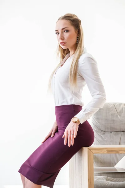 穿着紫色裙子和白色衬衣的性感金发女孩的肖像坐在木桌上的现代办公室内饰 — 图库照片