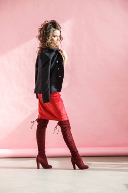 Moda stüdyo kırmızı etek, siyah ceket ve pembe arka plan üzerinde duran siyah iç çamaşırı giyen güzel kıvırcık kadın portresi