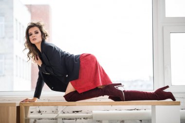 Gün ışığında ahşap pencere yatan kırmızı etek, siyah ceket ve siyah iç çamaşırı giyen güzel kıvırcık kadın moda studio portresi
